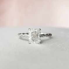 an engagement ring with a square cut diamond in the center and twisted band around it