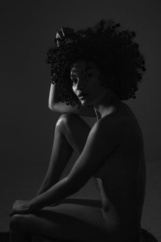 a naked woman sitting on the ground with her hair blowing in the wind, black and white photo