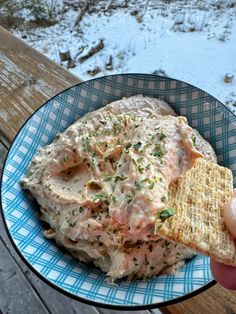 a person is holding a cracker over a bowl of food on a wooden table