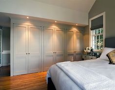 a large white bed sitting in a bedroom next to a wooden floor and two windows