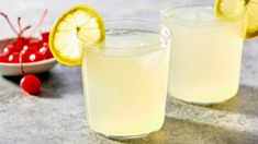 two glasses filled with lemonade next to a bowl of cherries and a cherry