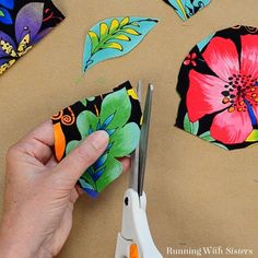 someone using scissors to cut fabric with colorful flowers on the top and bottom of them