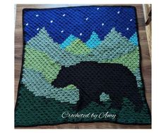 a crocheted blanket with a black bear on it and mountains in the background