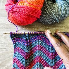 a hand is knitting yarn on top of a wooden table