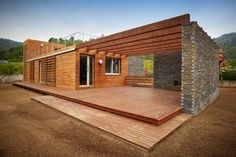 a house made out of wood and stone sitting on top of a dirt field next to a wooden deck