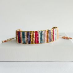 a bracelet with multicolored beads is sitting on top of a white surface and has a gold chain