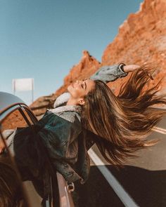 a woman with long hair leaning out the window of a car on a desert road