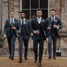 three men in suits and ties are walking with wine glasses on their feet while one man is wearing a suit