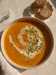 a bowl of carrot soup with bread on the side