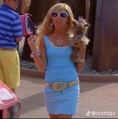 a woman in a blue dress holding a small dog on her hip while standing next to a pink car