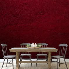 a wooden table with four chairs in front of a red wall that has a candle on it