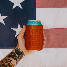 a person holding a can of drink in front of an american flag with the words drink more beer on it