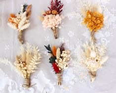 six dried flowers are arranged on a white tablecloth with floral designs in the background