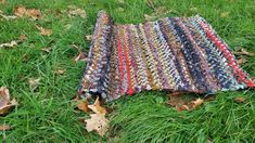 a multicolored rug is laying in the grass on top of some fallen leaves