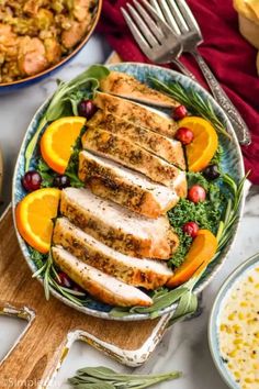 sliced chicken on a plate with oranges and cranberries next to other dishes