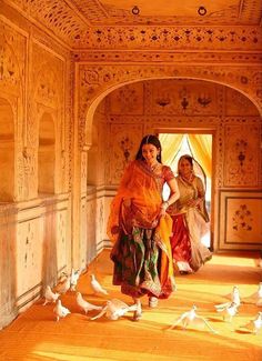 two women are walking through an archway with birds around them