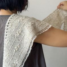 a woman wearing a white knitted shawl over her shoulder and holding onto the back of her arm