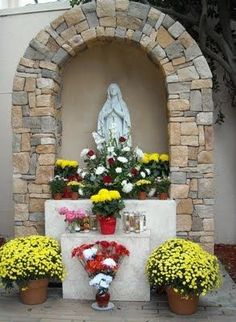 flowers are placed in front of a stone arch with a statue behind it and potted plants on either side