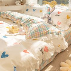 a bed with white sheets and colorful hearts on it, next to a stuffed animal