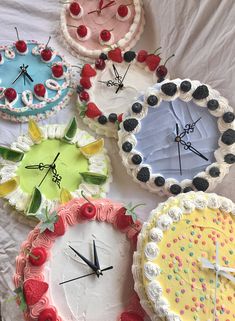 four cakes with different designs on them sitting on a white sheet covered tablecloth, all decorated in various colors and sizes