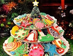 three tiered trays filled with decorated cookies on top of a green christmas tree