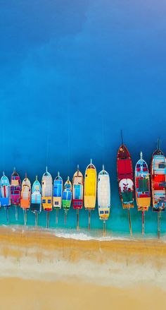 a row of colorful boats sitting on top of a sandy beach next to the ocean