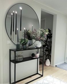 a black and white console table with flowers on it in front of a round mirror