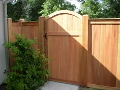 a wooden gate in front of a house next to a green bush and shrubbery