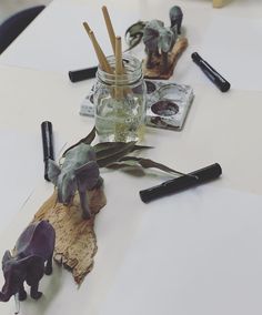 some glass jars filled with plants on top of a white table covered in writing utensils