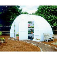 a small white building sitting on top of a dirt field next to trees and flowers