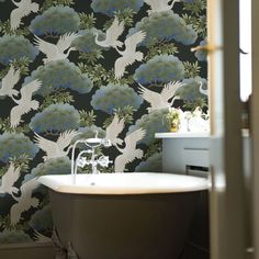 a bath tub sitting under a window next to a wallpaper covered in white birds