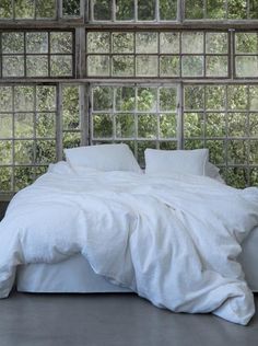 a bed with white linens and pillows in front of a window that has glass panes