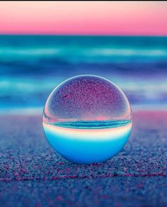 a glass ball sitting on top of a sandy beach next to the ocean at sunset