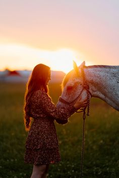 a woman is petting a white horse at sunset