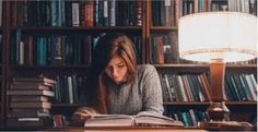 a woman sitting at a table in front of a bookshelf reading a book