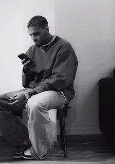 a black and white photo of a man sitting on a chair holding a cell phone