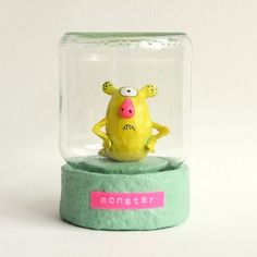 a yellow toy sitting inside of a glass jar on top of a green base with a pink name tag