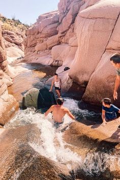 three people are playing in the water near some rocks