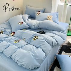 a bed with blue comforters and pillows on top of it next to a teddy bear