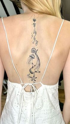 the back of a woman's white dress with tattoos on her upper and lower back