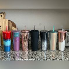 there are many different colored cups lined up on the kitchen counter top, and one has a straw in it