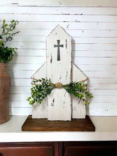 a white wooden house with a cross on it and some greenery in the corner