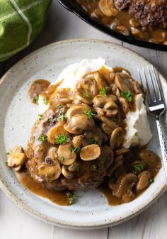 a white plate topped with mashed potatoes covered in mushroom gravy and mushrooms