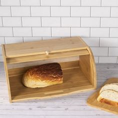 a loaf of bread sitting in a wooden box next to a slice of bread on a cutting board