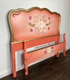 a pink bench with gold trim and flowers painted on the back, against a white wall