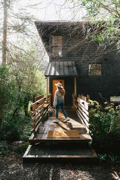 a woman walking across a wooden bridge in front of a black building with a metal roof