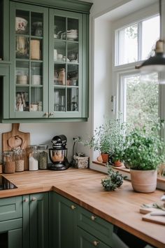 a kitchen with green cupboards and wooden counter tops next to a potted plant