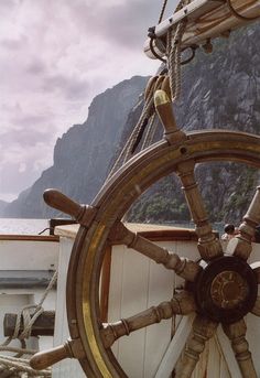 an image of a boat steering wheel with mountains in the back ground and water behind it