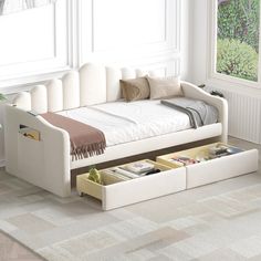 a white daybed with drawers underneath it in a room next to a window and rug