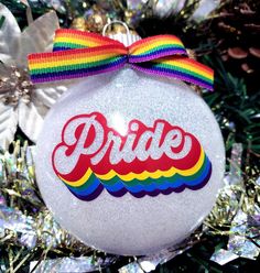 a christmas ornament with the word pride painted on it and a rainbow ribbon